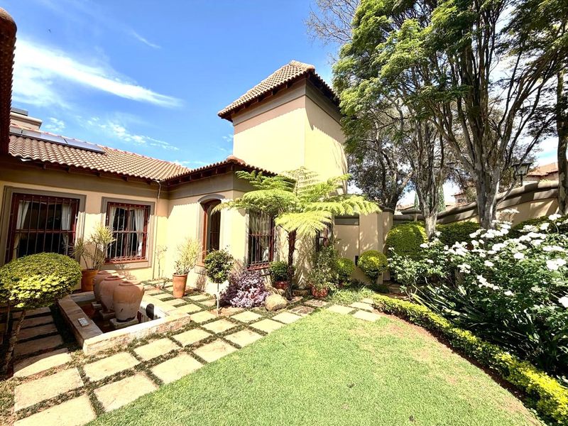 A well-maintained rear garden featuring a stone-paved walkway, a decorative water feature, and established landscaping against the house exterior.