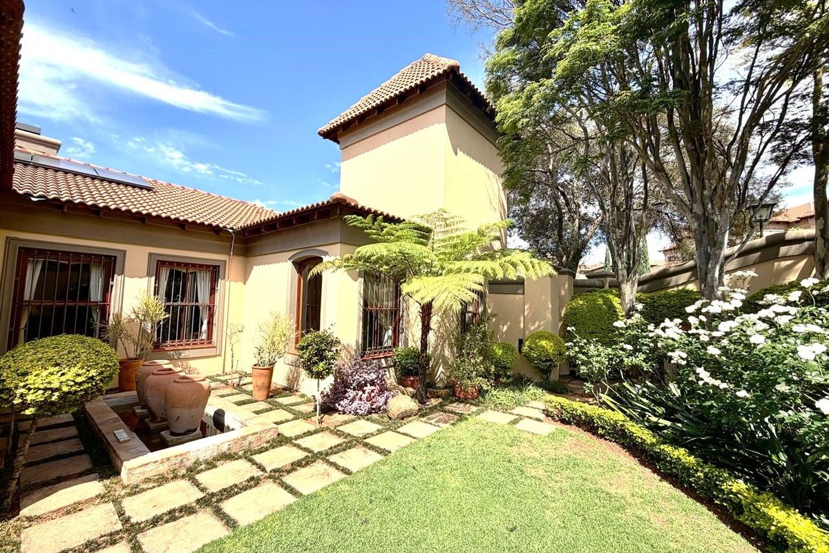 A well-maintained rear garden featuring a stone-paved walkway, a decorative water feature, and established landscaping against the house exterior.