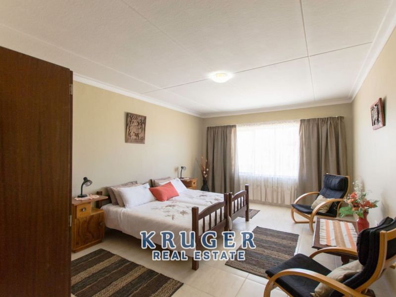 A spacious bedroom featuring tiled flooring, neutral wall finishes, and a large window with curtaining.