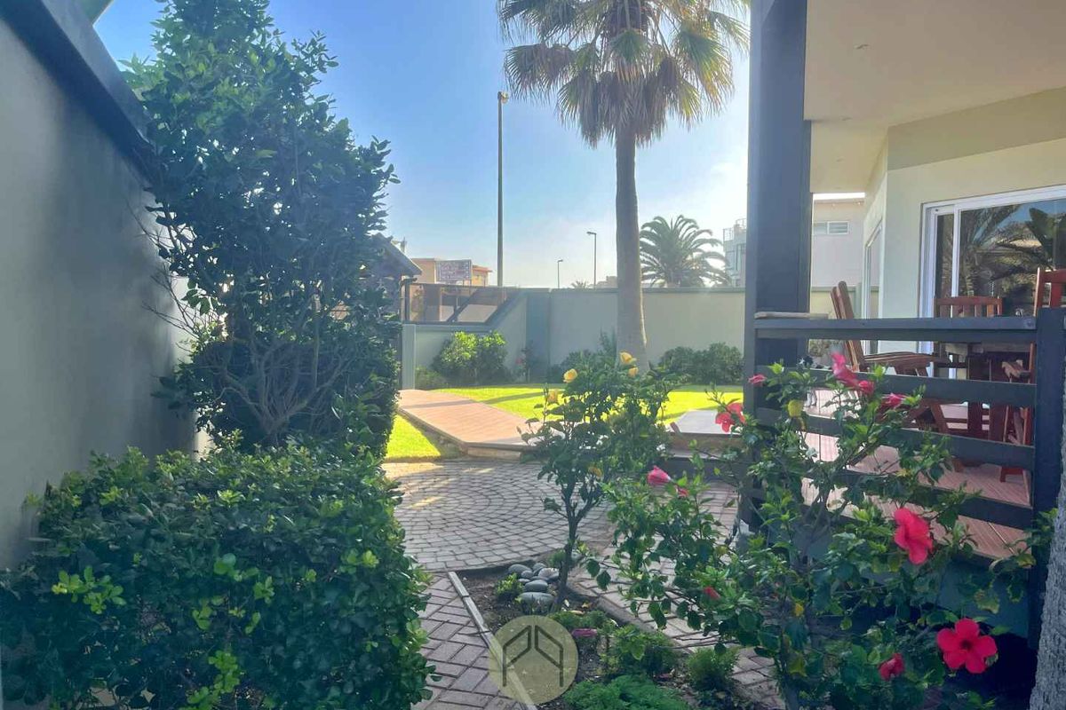 A well-maintained rear garden featuring a paved circular patio area, lush lawn, and established landscaping, adjacent to a covered patio space.