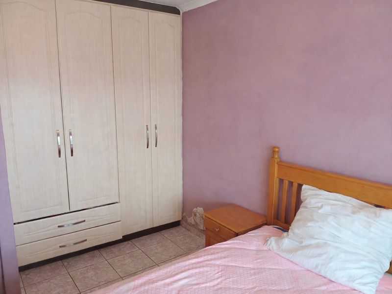 A bedroom featuring built-in wardrobes and tiled flooring, showing visible signs of wall plaster damage near the baseboard.