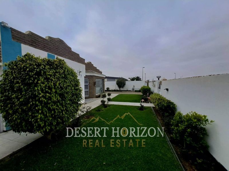 A well-maintained rear garden featuring a manicured lawn, paved walkway, and perimeter boundary wall, providing a private outdoor space.