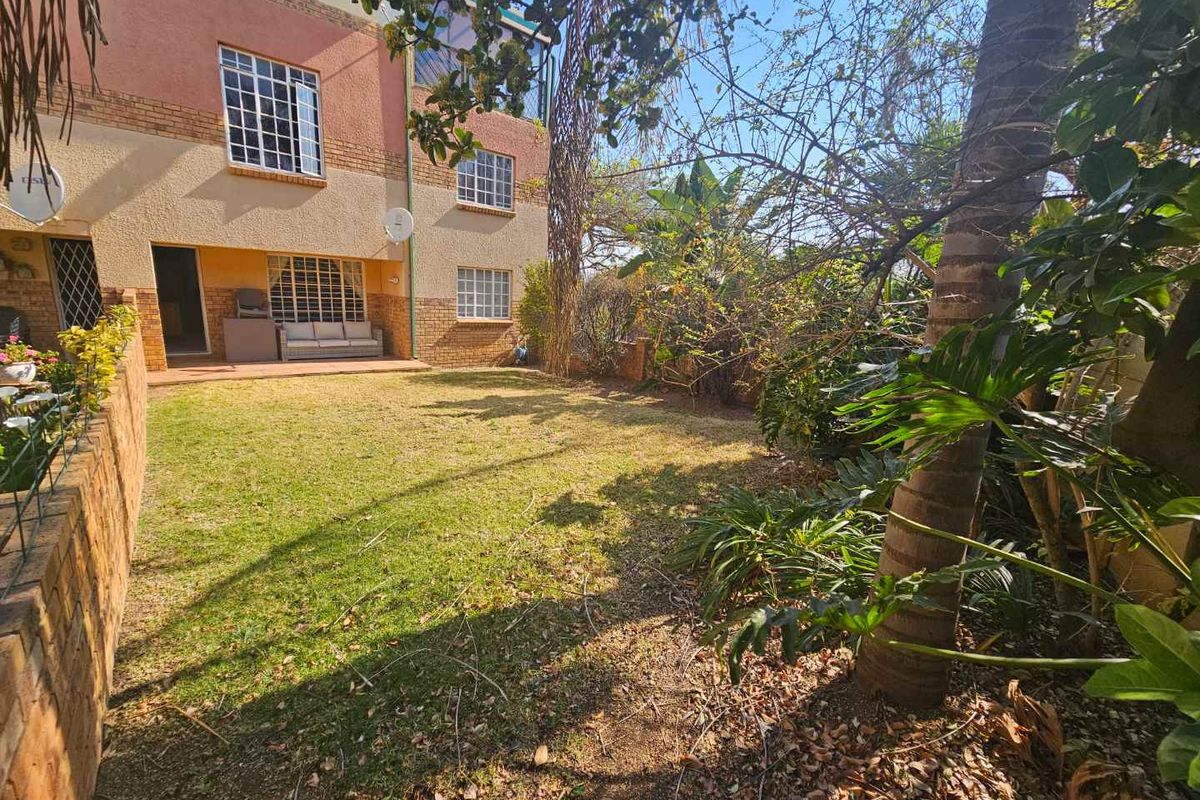A rear view of the apartment building featuring a private garden, paved patio area, and established landscaping.