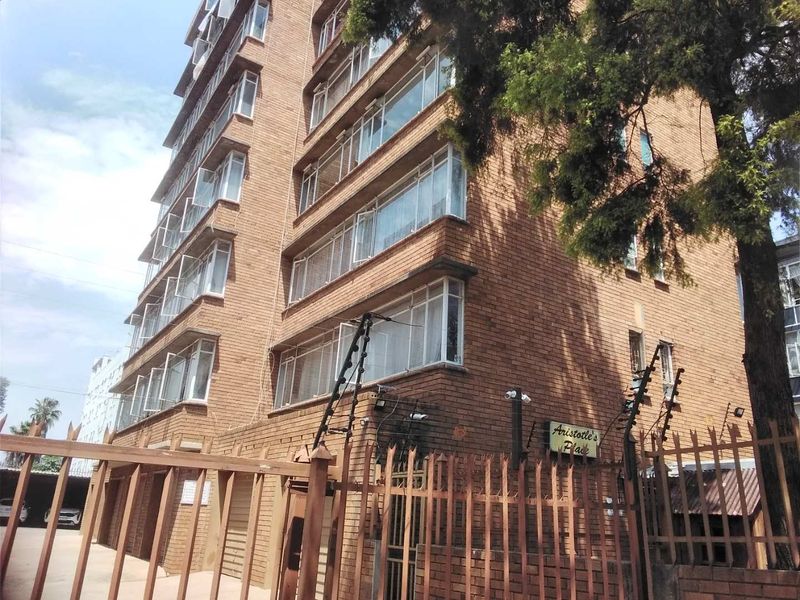 Exterior view of a multi-story brick apartment building featuring casement windows, secure perimeter fencing, and integrated security systems.