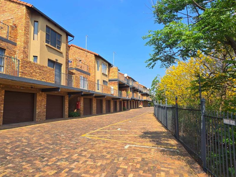 Exterior view of a townhouse complex featuring a paved driveway, multiple roller garage doors, and brick facade architecture.