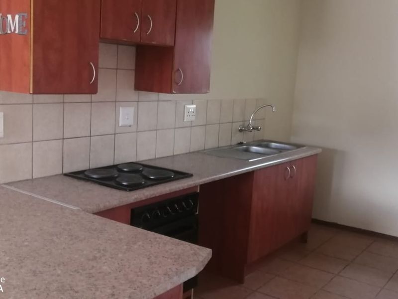 A functional kitchen featuring built-in wooden cabinetry, laminate countertops, an electric hob, oven, and a double sink with tiled backsplash and flooring.