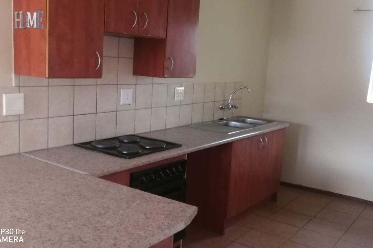A functional kitchen featuring built-in wooden cabinetry, laminate countertops, an electric hob, oven, and a double sink with tiled backsplash and flooring.