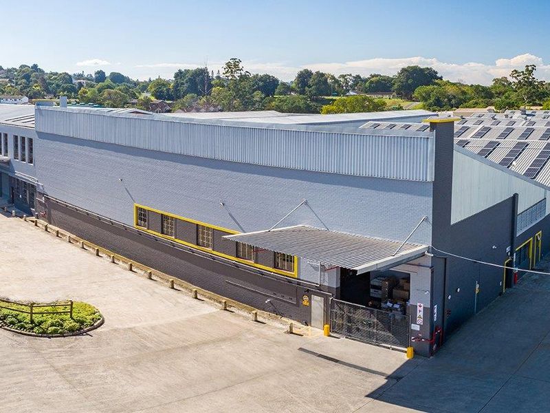 Aerial view of an industrial warehouse facility featuring a large concrete yard, loading bay access, and extensive roof-mounted solar panels.