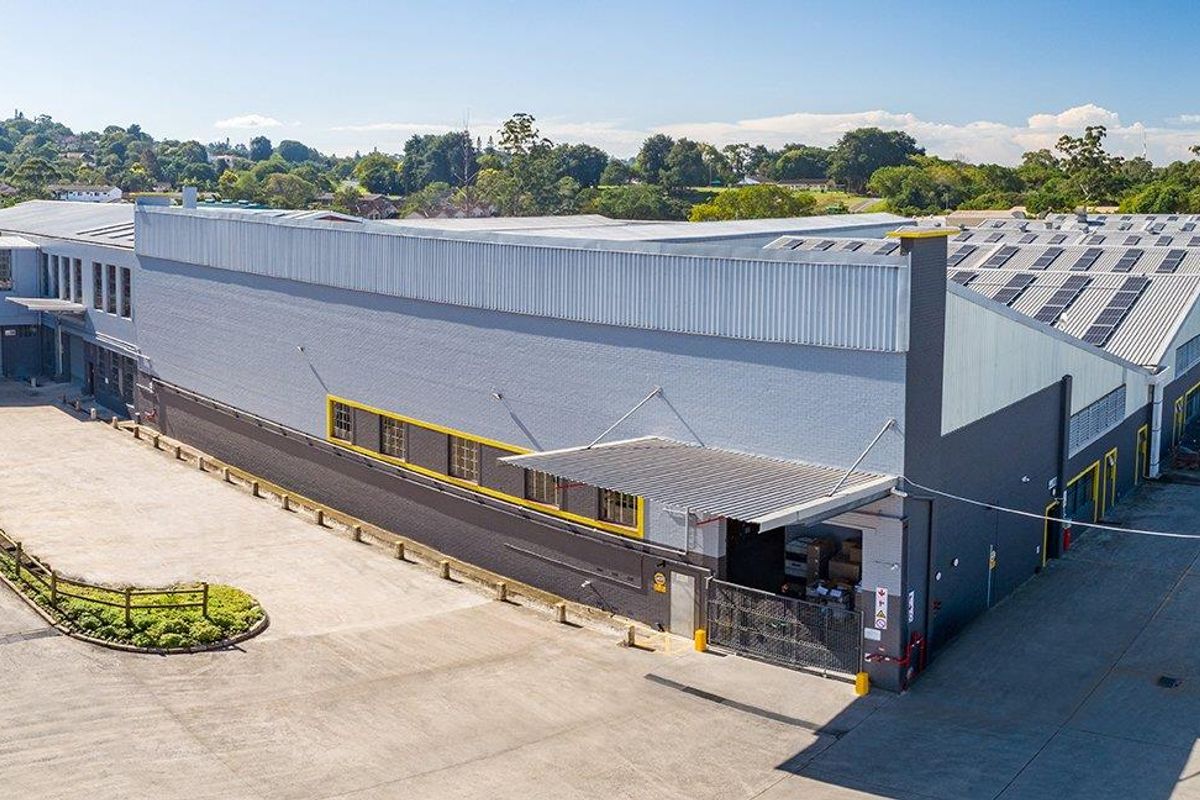 Aerial view of an industrial warehouse facility featuring a large concrete yard, loading bay access, and extensive roof-mounted solar panels.
