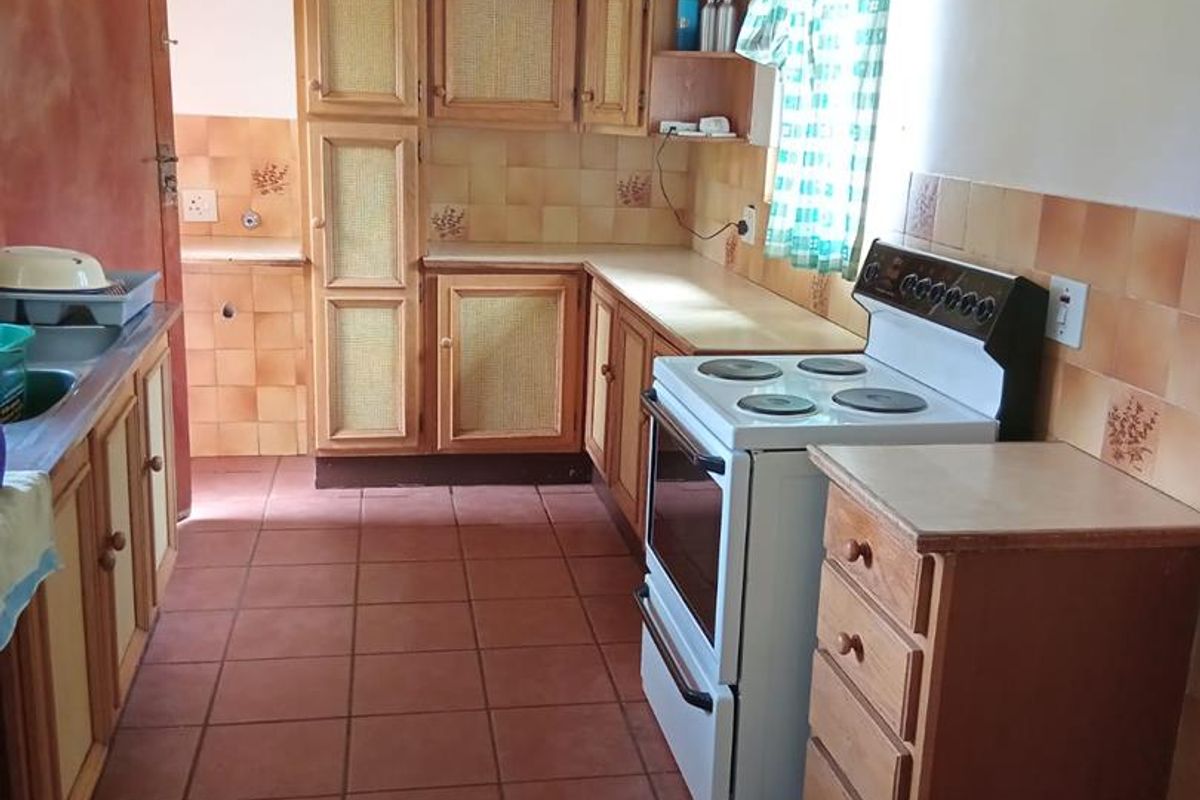 A dated kitchen featuring wooden cabinetry, tiled splashbacks, terracotta floor tiles, and a freestanding electric stove.