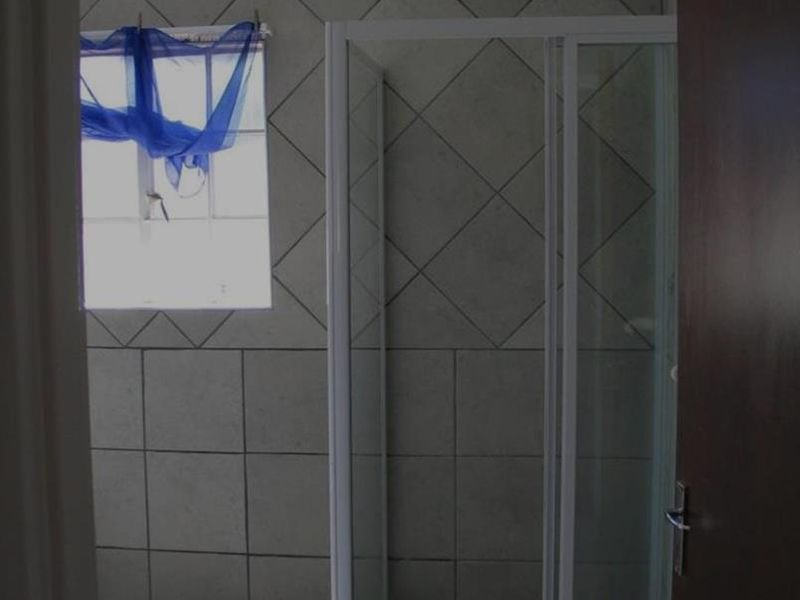 A functional bathroom featuring a glass shower enclosure, neutral wall and floor tiling, and a window for natural light.