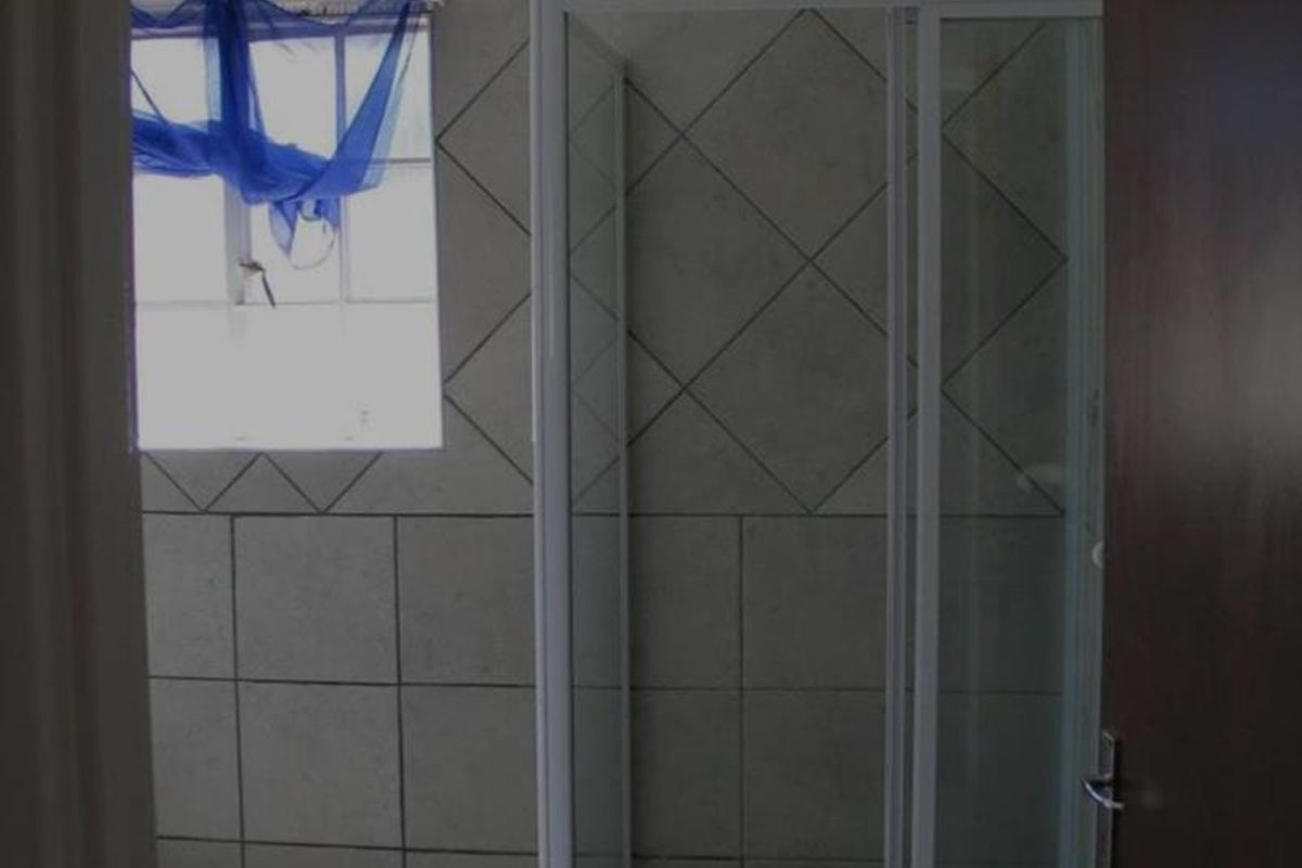 A functional bathroom featuring a glass shower enclosure, neutral wall and floor tiling, and a window for natural light.