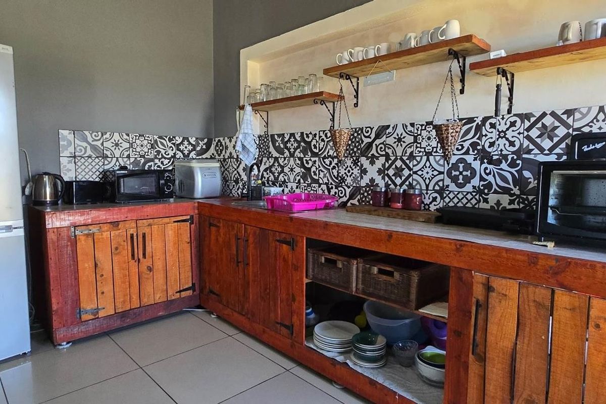 A rustic-style kitchen featuring custom timber cabinetry, patterned tile backsplash, open shelving, and tiled flooring.
