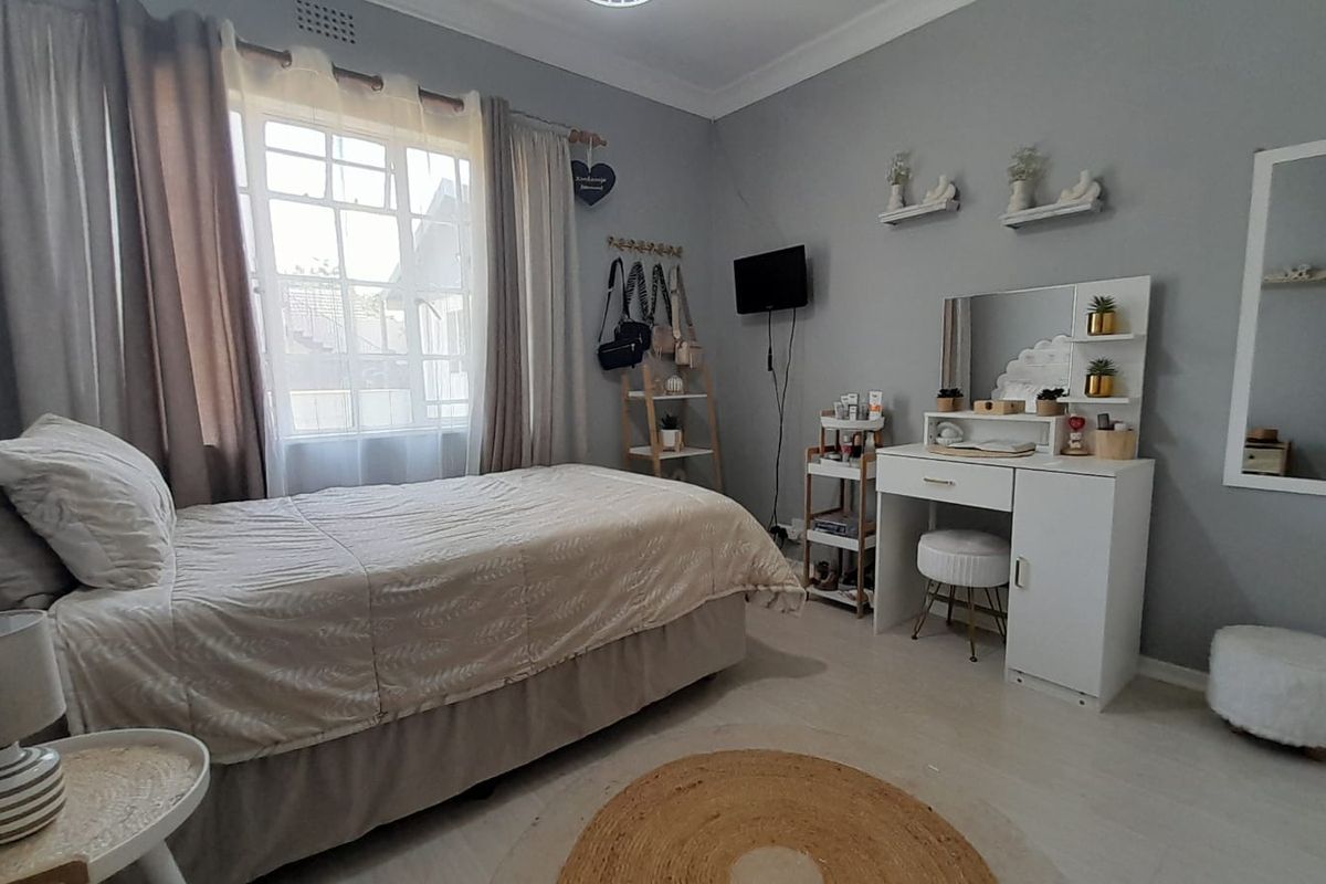 A well-maintained bedroom featuring neutral grey walls, a large window with natural light, and classic cornice detailing.