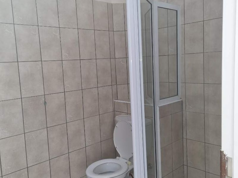 A functional bathroom featuring a corner shower enclosure with a glass door and a standard toilet, finished with neutral wall and floor tiling.