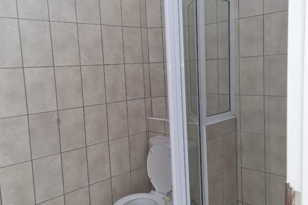 A functional bathroom featuring a corner shower enclosure with a glass door and a standard toilet, finished with neutral wall and floor tiling.