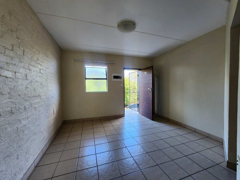 An empty entrance area featuring tiled flooring, an exposed brick feature wall, and a secure entrance door with an integrated security gate.