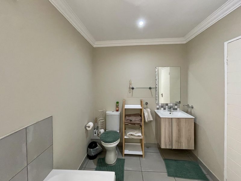 A functional bathroom featuring a wall-mounted vanity with basin, a toilet, and neutral wall finishes with tiled flooring.