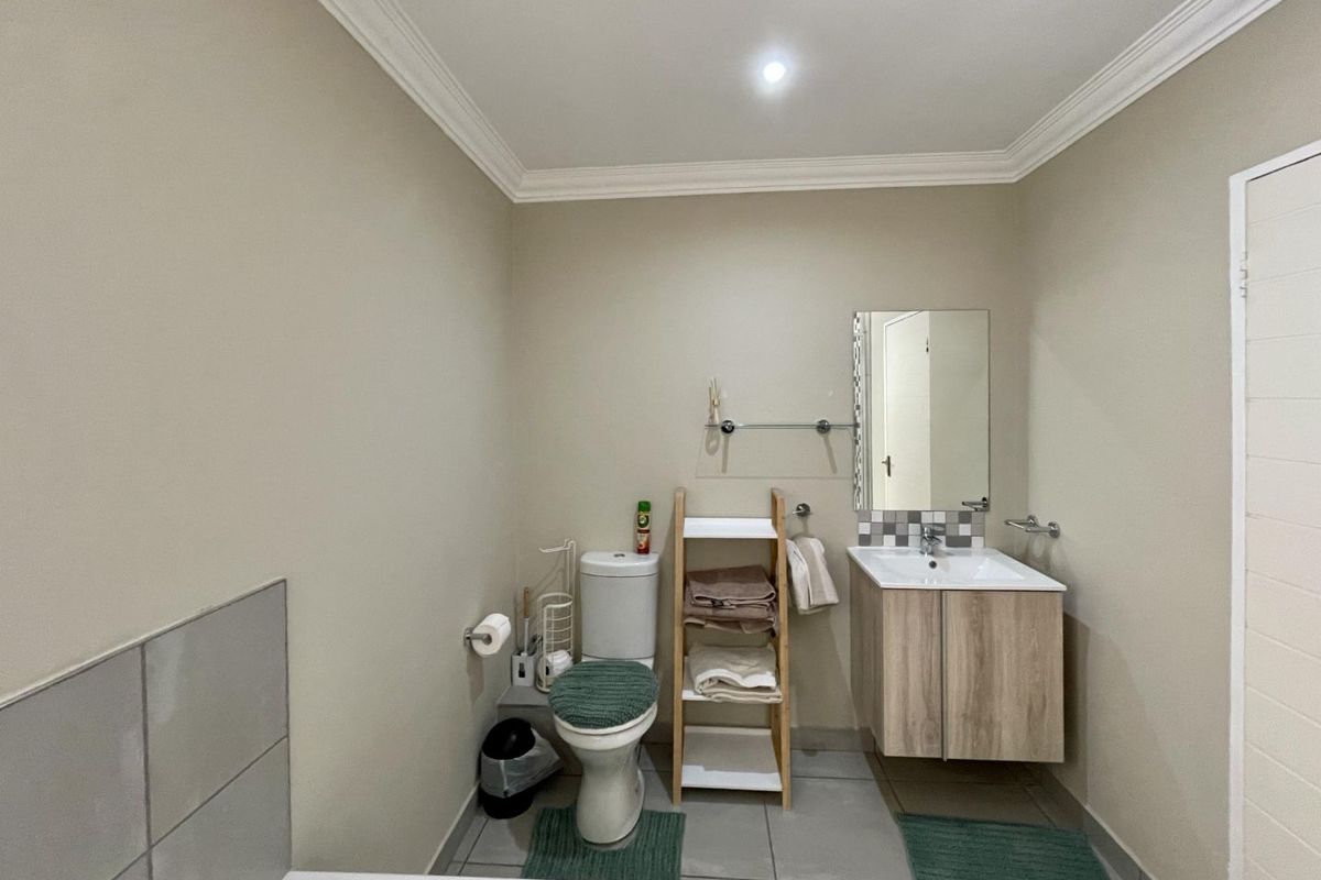 A functional bathroom featuring a wall-mounted vanity with basin, a toilet, and neutral wall finishes with tiled flooring.