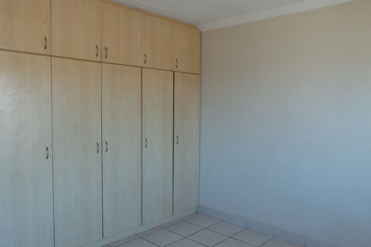 A bedroom featuring built-in wooden cupboards with overhead storage and tiled flooring.