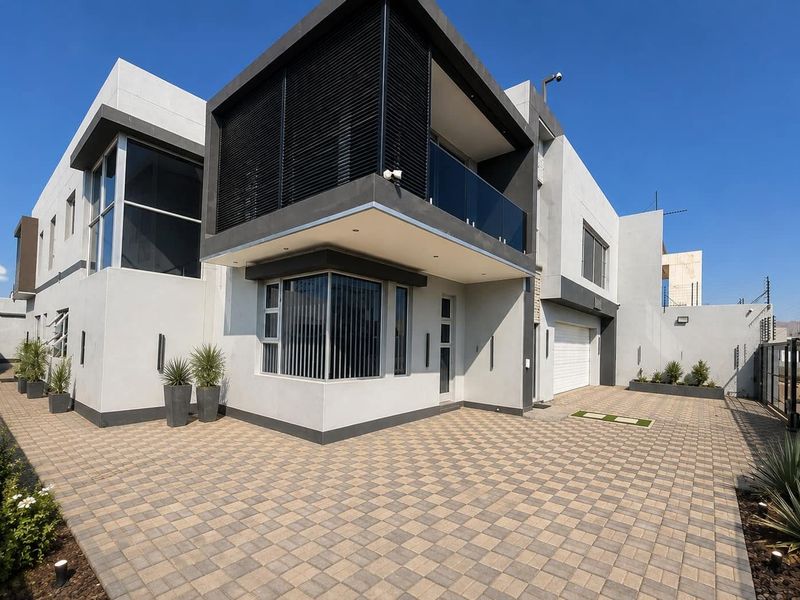 Modern double-story residence featuring a paved driveway, integrated double garage, and a sleek balcony with glass balustrades and security shutters.