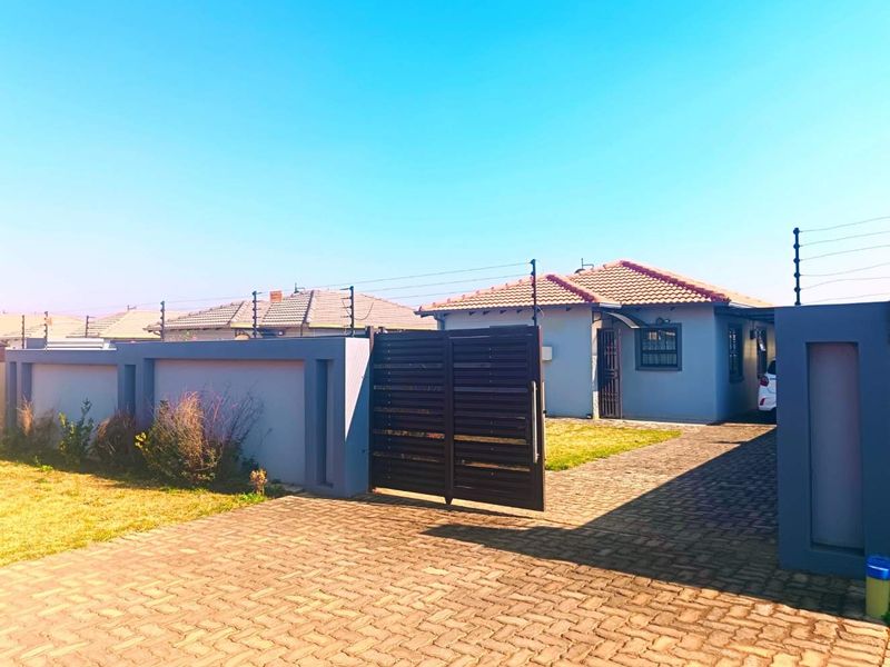 Front view of a residential property featuring a paved driveway, secure perimeter wall with electric fencing, and a gated entrance.