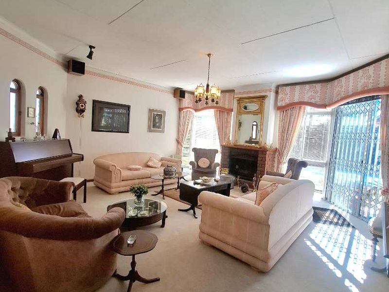 Spacious living room featuring a brick fireplace, central skylight, and large windows with security gates, offering a traditional layout with potential for modernization.