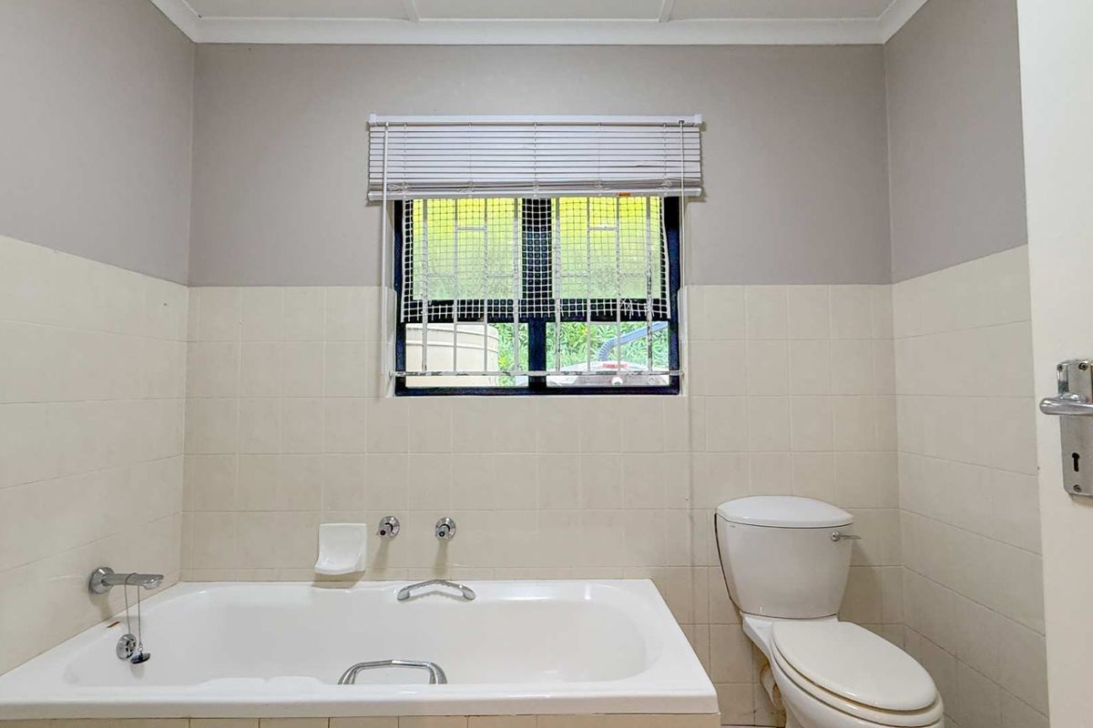 A functional bathroom featuring a built-in bathtub, a standard toilet, and tiled wall finishes with a window providing natural light.