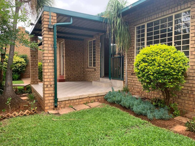 A covered brick patio area with tiled flooring, featuring security gates and window bars, overlooking a small garden space.
