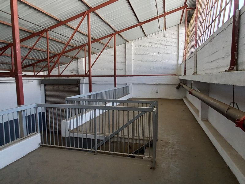 An industrial mezzanine level featuring exposed steel roof trusses, painted brick walls, metal railings, and concrete flooring, suitable for storage or workspace.