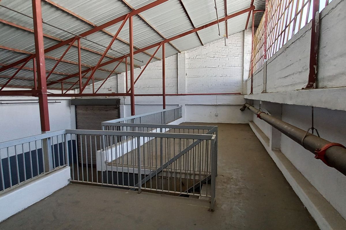 An industrial mezzanine level featuring exposed steel roof trusses, painted brick walls, metal railings, and concrete flooring, suitable for storage or workspace.