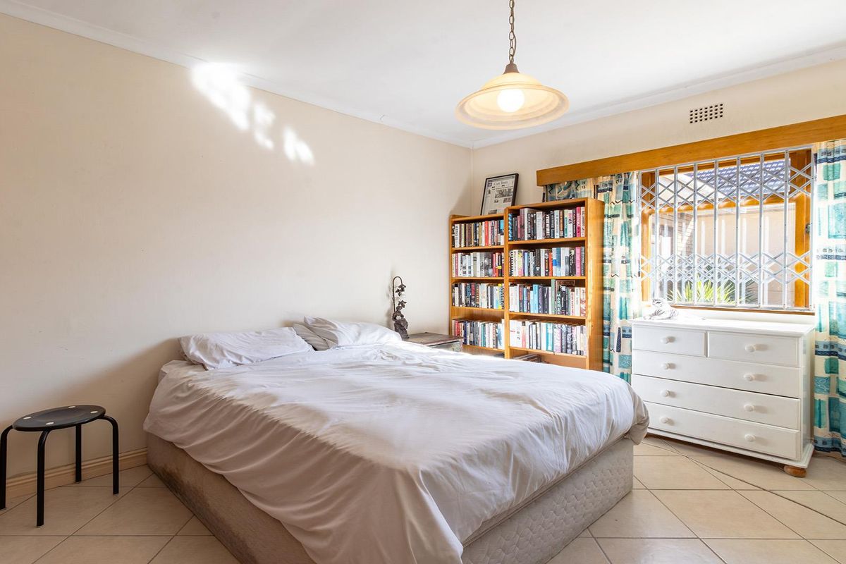 A functional bedroom featuring tiled flooring, a pendant light fixture, and a window fitted with a security gate.