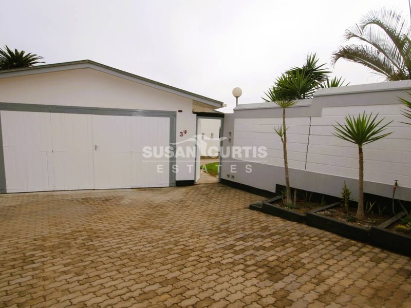 Front exterior view of the property featuring a paved driveway, a single garage, and a secure boundary wall with a pedestrian entrance.