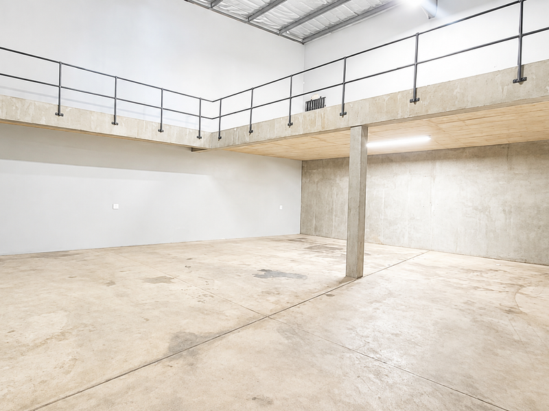 Spacious industrial utility area featuring a mezzanine level, concrete flooring, and metal staircase access, suitable for storage or workshop use.