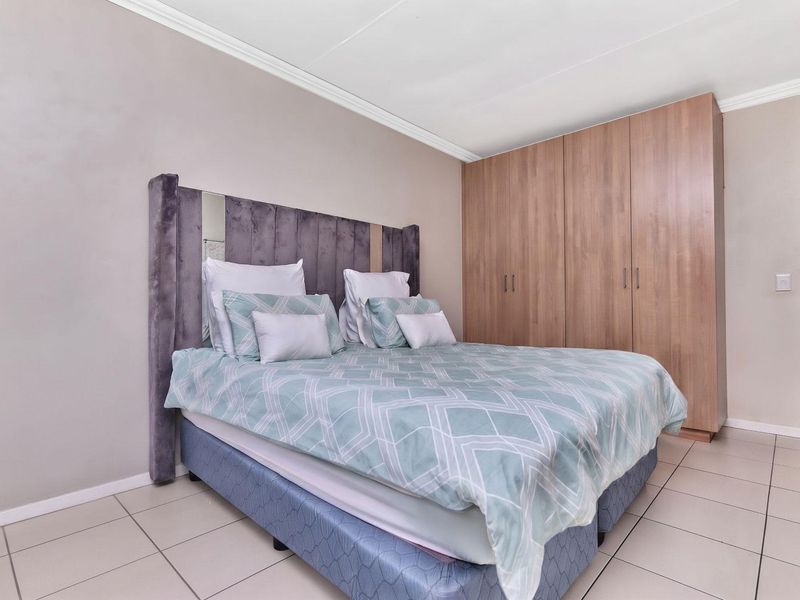 A well-maintained bedroom featuring neutral wall tones, tiled flooring, coved ceilings, and ample built-in wooden cupboards for storage.
