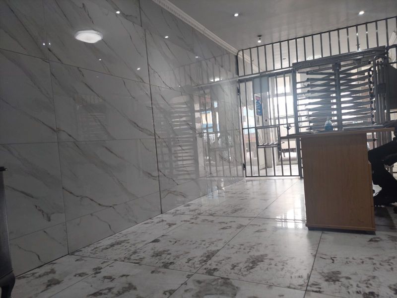 A modern entrance area featuring polished marble-effect wall and floor tiles, recessed lighting, and a secure metal gate entrance.