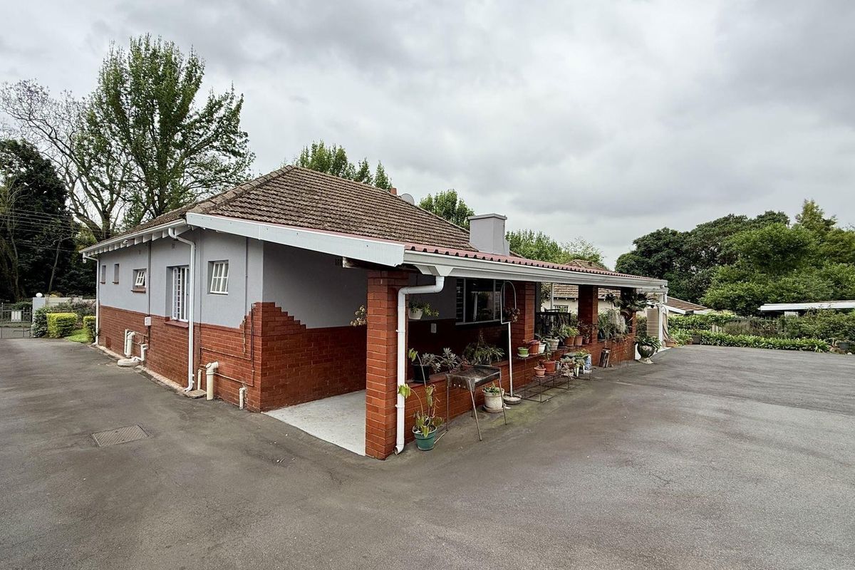 A view of the rear exterior of the house featuring a covered patio area, brick and rendered walls, and a tiled roof.