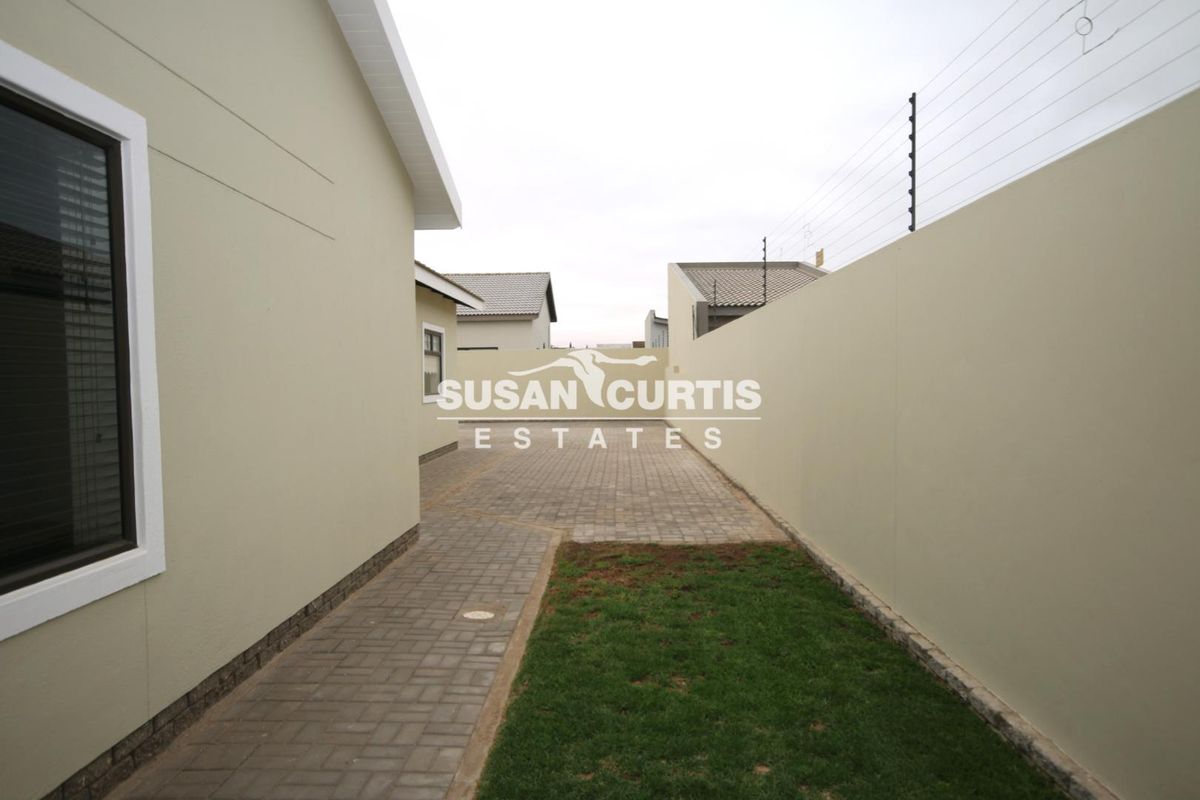 A side view of the property featuring a paved walkway, a small lawn area, and secure boundary walls with electric fencing.