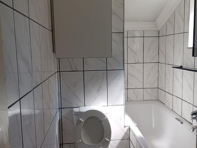 A compact bathroom featuring white marble-effect wall tiles, a standard bathtub, and a wall-mounted storage cabinet under a sloped ceiling.