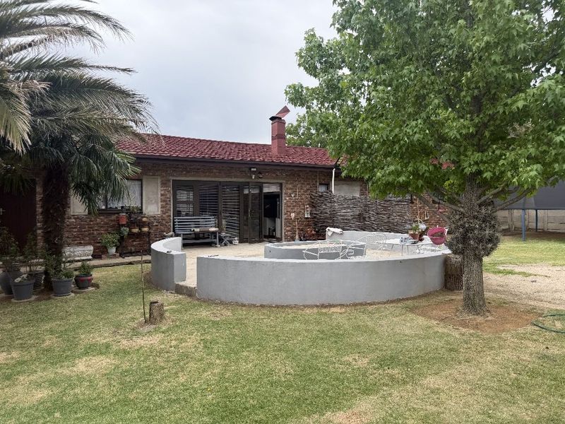 Rear view of the house featuring a brick facade, tiled roof, and a curved masonry patio area set within a spacious garden.
