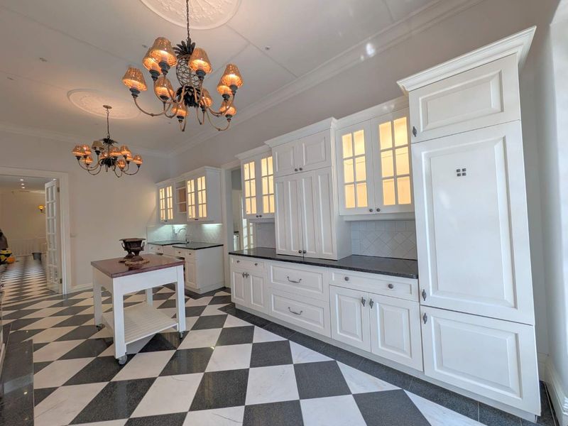 Elegant kitchen featuring custom white cabinetry, integrated appliances, dark stone countertops, and classic checkered marble flooring under decorative ceiling medallions.