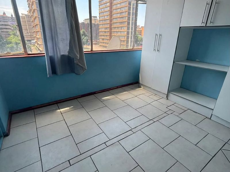 An empty bedroom featuring built-in cupboards, tiled flooring, and large windows with urban views, offering a blank canvas for renovation.