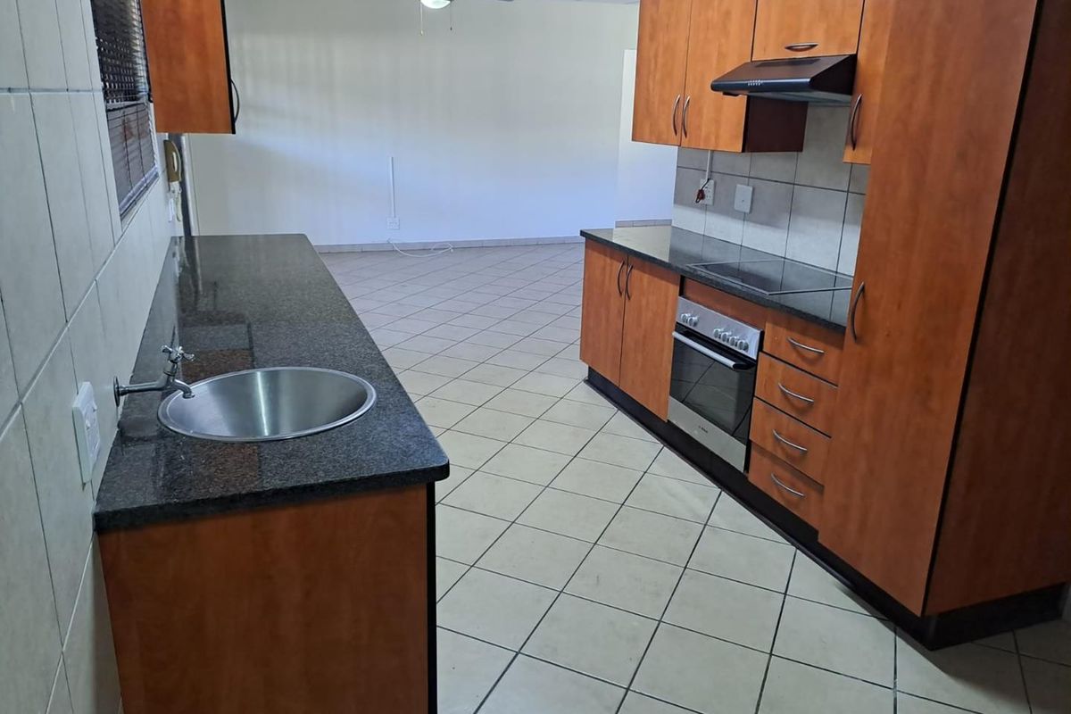 Open plan kitchen featuring granite countertops, built-in oven, hob, extractor fan, and tiled flooring, flowing into an adjacent living area.