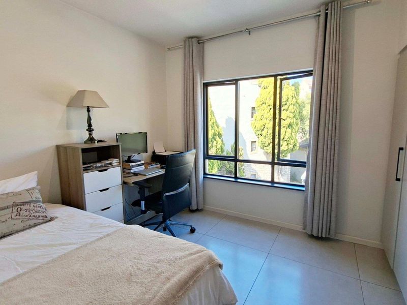 A well-lit bedroom featuring neutral tiled flooring, a large window with curtain tracks, and a built-in wardrobe for storage.