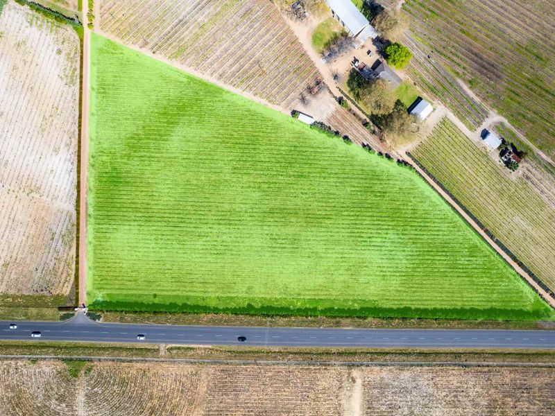 Aerial view of a large, triangular agricultural land parcel with direct road access and surrounding cultivated fields.