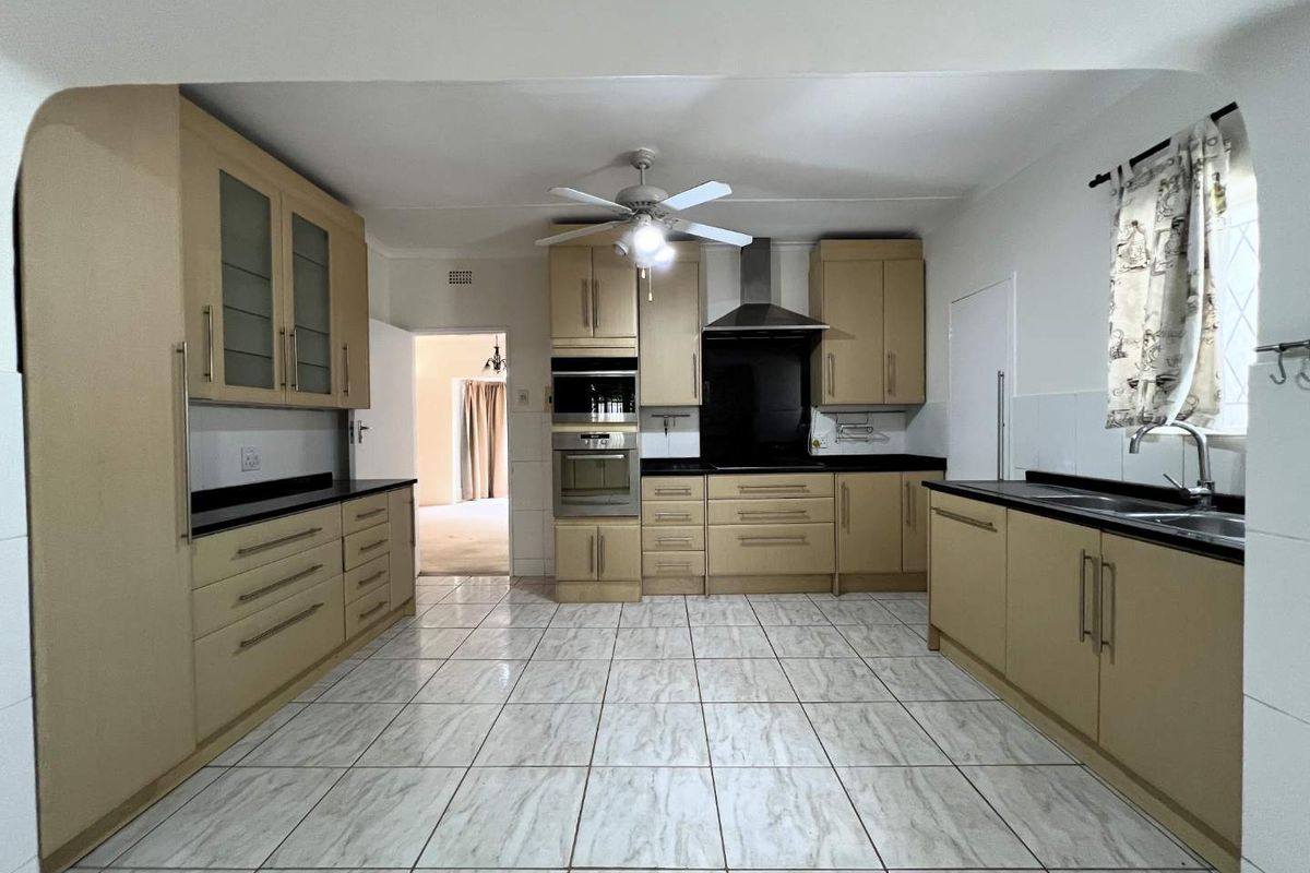 Spacious kitchen featuring light wood-toned cabinetry, dark stone countertops, built-in oven, extractor fan, and tiled flooring throughout.