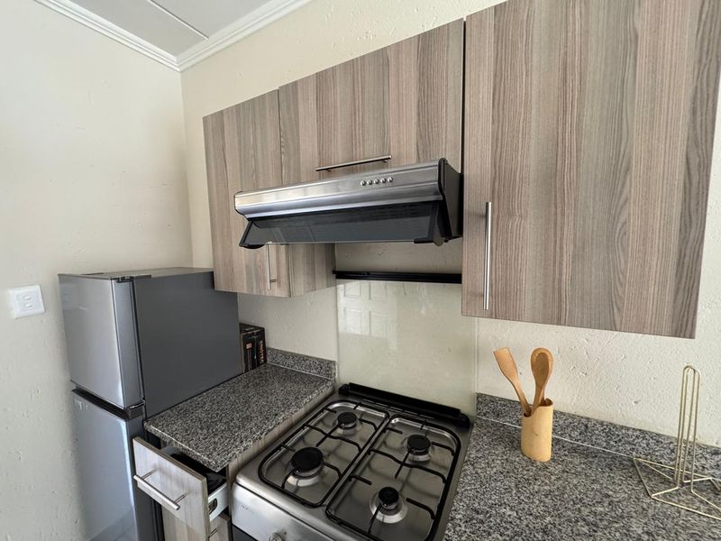 Compact kitchen featuring wood-grain cabinetry, granite countertops, a gas hob, and a stainless steel extractor fan with a glass splashback.