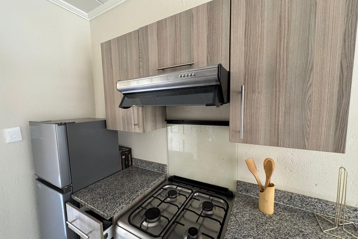 Compact kitchen featuring wood-grain cabinetry, granite countertops, a gas hob, and a stainless steel extractor fan with a glass splashback.
