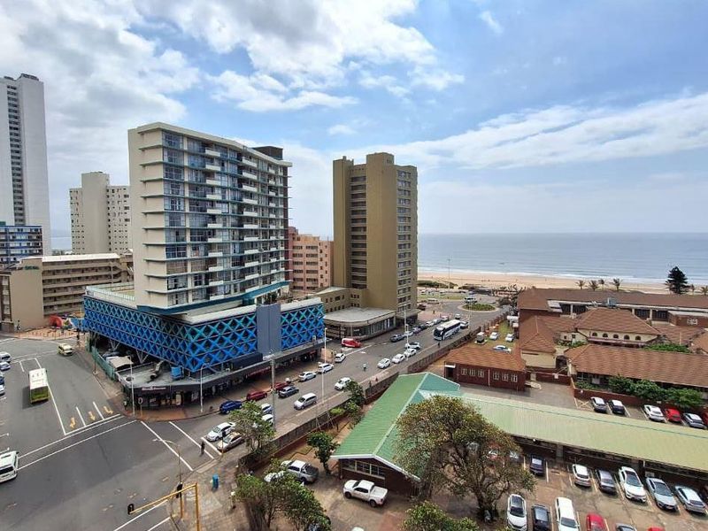 Elevated urban and coastal view overlooking surrounding high-rise apartment buildings, city streets, and the nearby beach coastline.
