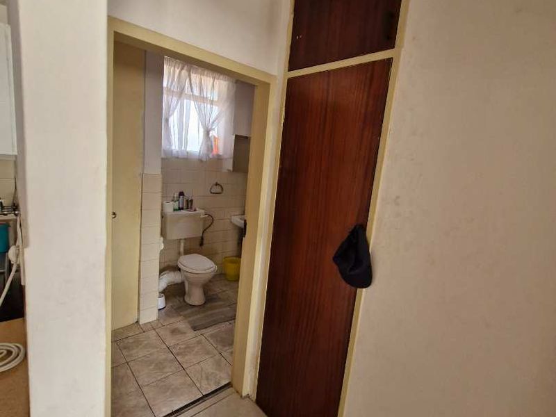 A functional hallway featuring tiled flooring and a built-in wooden cupboard, providing access to the adjacent bathroom area.